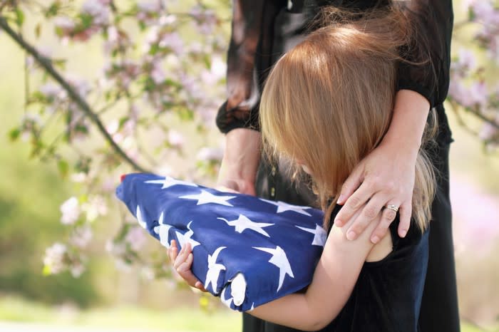 Little girl with mother's arm around her holding a folded American flag at a funeral.