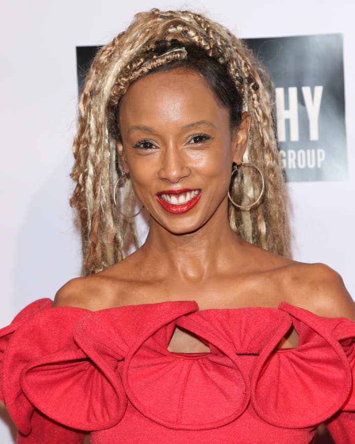 Trina McGee with loc'd hair in a off-the-shoulder dress with spiral ruffles smiles at the camera on a red carpet
