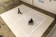 In this Nov. 17, 2019, photo provided by the University of Michigan, brothers Darren Kreps, left, and Bryan Kreps play a game modeled after soccer and air hockey using the iGYM system at the university in Ann Arbor, Mich. A University of Michigan research team has created iGYM, an augmented reality system that allows people with different levels of mobility to play and exercise together. (Roger Hart/University of Michigan via AP)