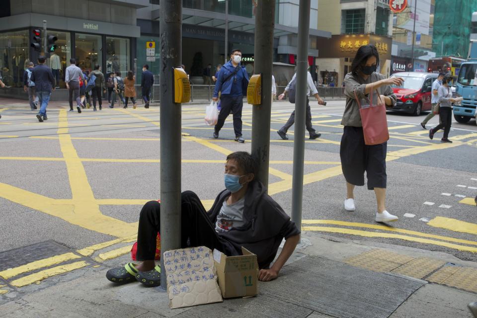 People wearing face masks walks past a beggar at a downtown street in Hong Kong, Thursday, April 8, 2021. (AP Photo/Vincent Yu)