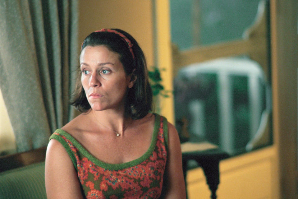 Frances McDormand wearing a vintage floral dress, seated indoors, looking pensive