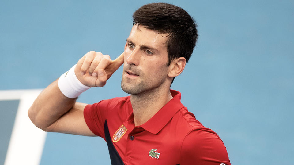 Novak Djokovic gestures towards his ear at the crowd.