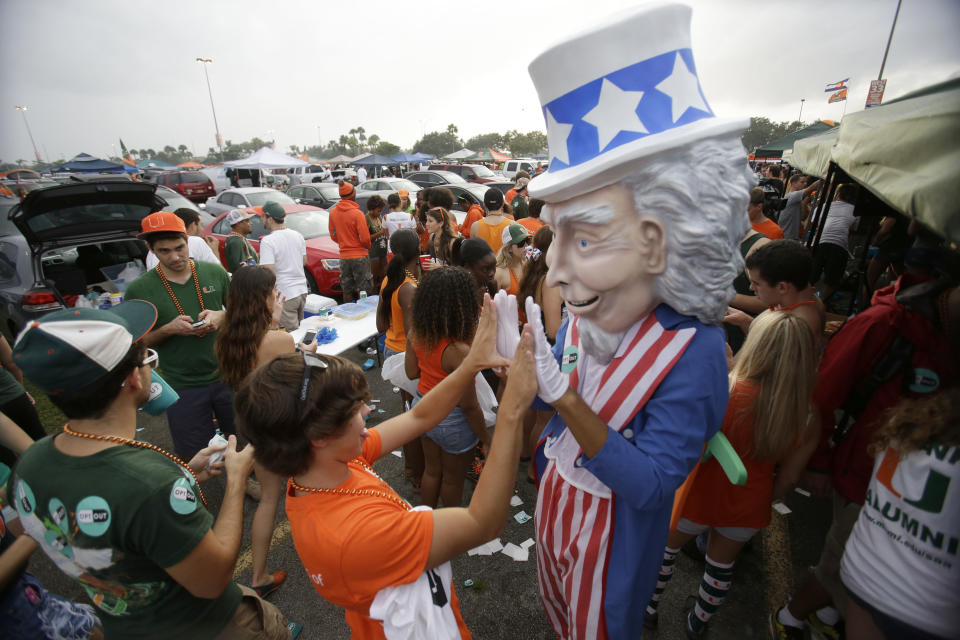In this Saturday, Nov. 9, 2013 photo, Thomas Vazquez, center left, 18, high-fives an Uncle Sam mascot while tailgating before the start of an NCAA college football game between Miami and Virginia Tech, in Miami Gardens, Fla. It may be the hottest tailgate party at the University of Miami's homecoming game, but the 100-yard stretch of free pizza and party tents set up by Generation Opportunity, a national conservative organization, is also a carefully crafted strategy aimed at getting students to opt out of President Barack Obama's controversial new health law. (AP Photo/Wilfredo Lee)