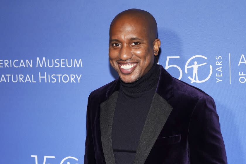 A bald man smiling in a dark velvet suit and turtleneck