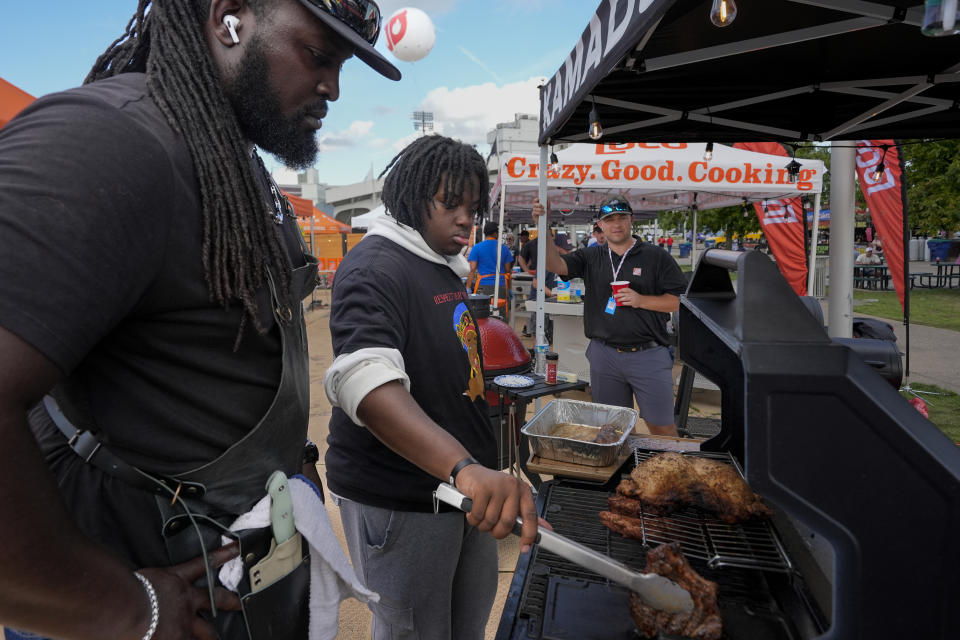 Rasheed Philips, left, teaches Eric Farley of the Boys and Girls Club how to sear a piece of grilled pork at the World Championship Barbecue Cooking Contest, Friday, May 17, 2024, in Memphis, Tenn. (AP Photo/George Walker IV)