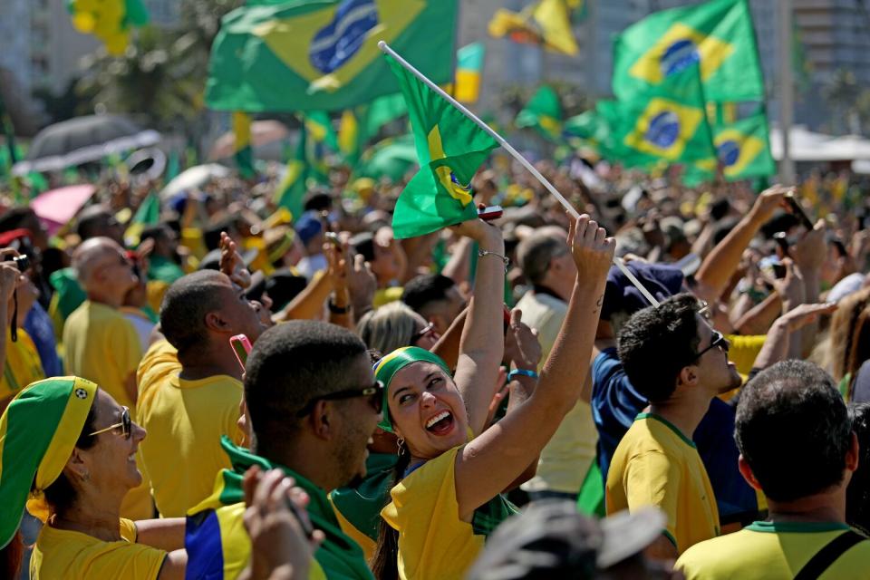 A woman holds up a green-and-yellow flag in a crowd of people waving similar flags