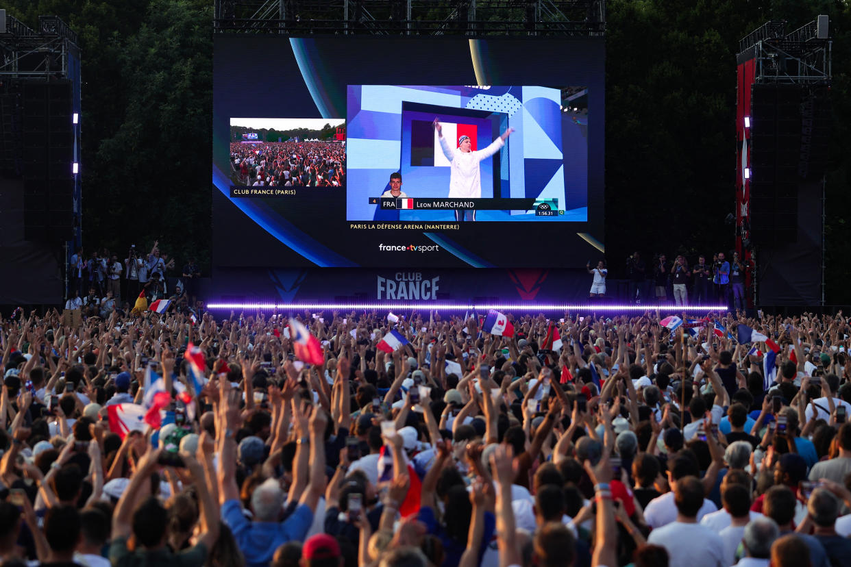 TOPSHOT - Supporters cheers as they watch on a giant screen France's Leon Marchand arriving for the final of the men's 200m individual medley swimming event during the Paris 2024 Olympic Games at the 