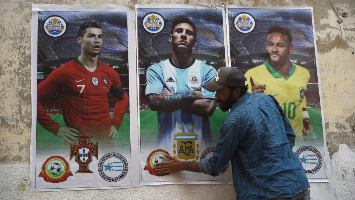 A football fan pastes posters of football players (L-R) Portugal's Cristiano Ronaldo, Argentina's Leo Messi and Brazil's Neymar Jr. on a wall ahead of the Qatar 2022 FIFA World Cup football tournament, in Karachi on November 12, 2022. (Photo by Rizwan TABASSUM / AFP)