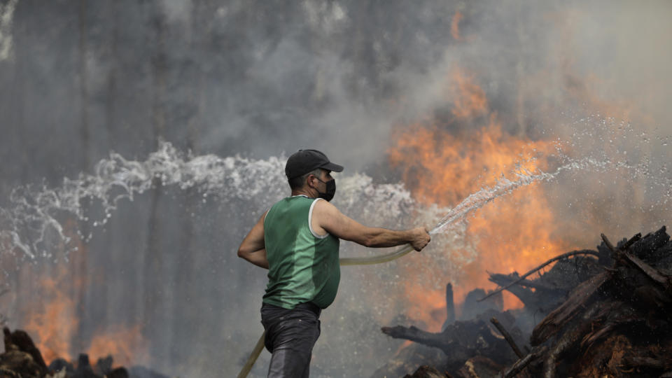 A local resident uses a garden hose to try to stop a forest fire from reaching houses in the village of Figueiras, outside Leiria, central Portugal, Tuesday, July 12, 2022. Hundreds of firefighters in Portugal continue to battle fires in the center of the country that forced the evacuation of dozens of people from their homes mostly in villages around Santarem, Leiria and Pombal. (AP Photo/Joao Henriques)