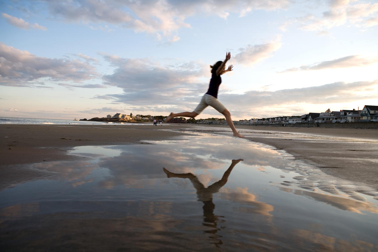 Woman leaping over puddle on beach (Jupiter images / Getty Images)