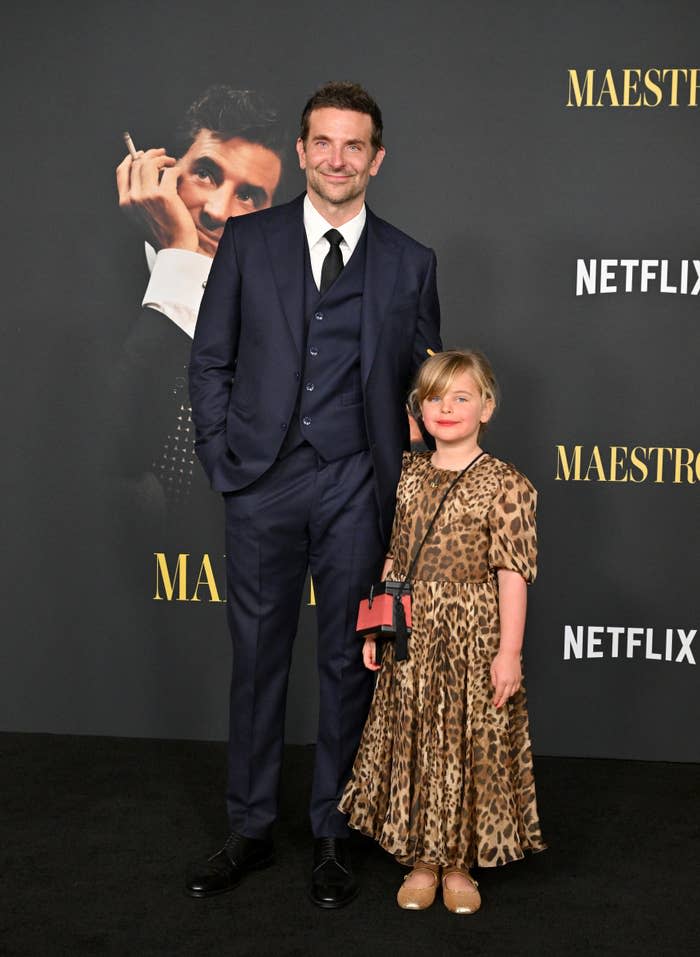 Bradley Cooper in a suit with his daughter who's wearing a leopard print dress at the "Maestro" Netflix event