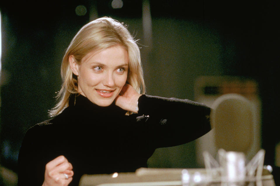 Cameron Diaz smiling and posing with a hand behind her neck, wearing a black turtleneck sweater indoors