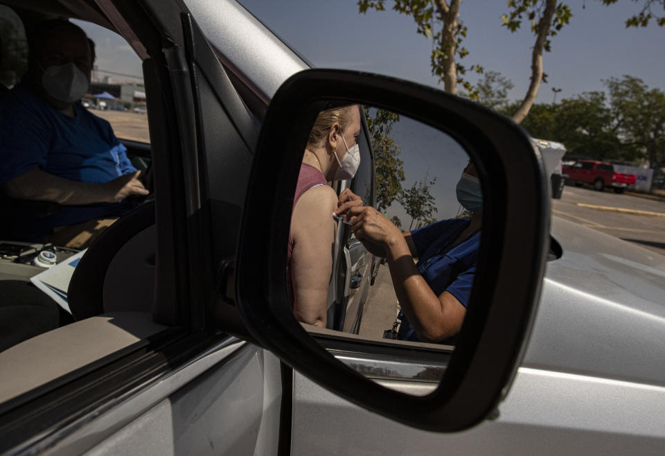 A woman is reflected in a side view car mirror as she is injected with her second dose of the Sinovac COVID-19 vaccine at a drive-thru vaccination site on the grounds of the National Stadium in Santiago, Chile, Wednesday, March 10, 2021. (AP Photo/Esteban Felix)