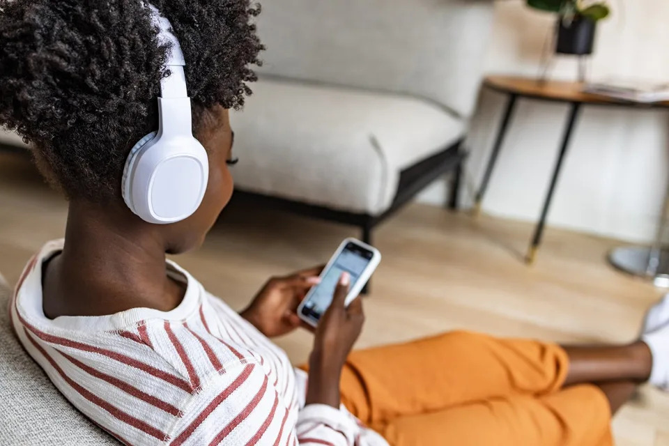 Young pistillate   sitting connected  the floor, utilizing mobile telephone  and listening euphony  via wireless headphones connected to her astute  phone