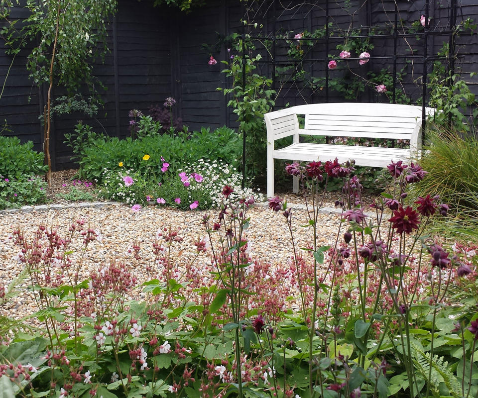 gravel patio area with a white bench surrounded by planting