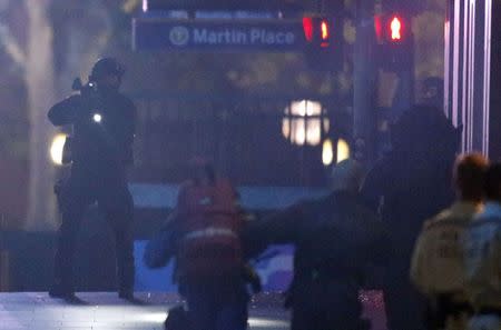 A heavily armed policeman holds his weapon as paramedics rush towards the Lindt cafe, where hostages are being held, at Martin Place in central Sydney December 16, 2014. REUTERS/Jason Reed