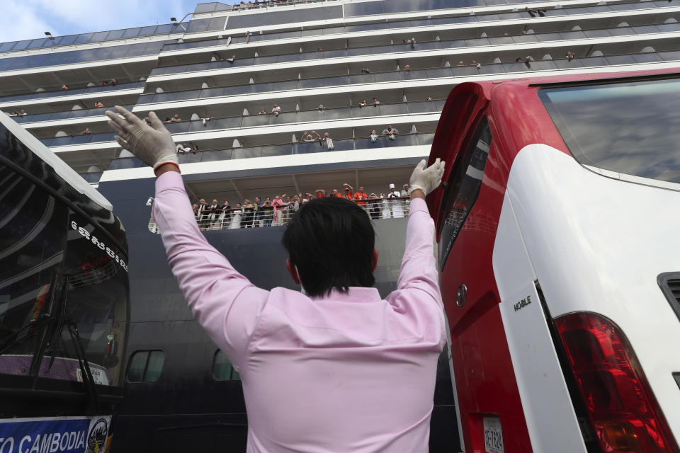 A man waves to passengers of the MS Westerdam, owned by Holland America Line, docked at the port of Sihanoukville, Cambodia, Friday, Feb. 14, 2020. Hundreds of cruise ship passengers long stranded at sea by virus fears cheered as they finally disembarked Friday and were welcomed to Cambodia. (AP Photo/Heng Sinith)