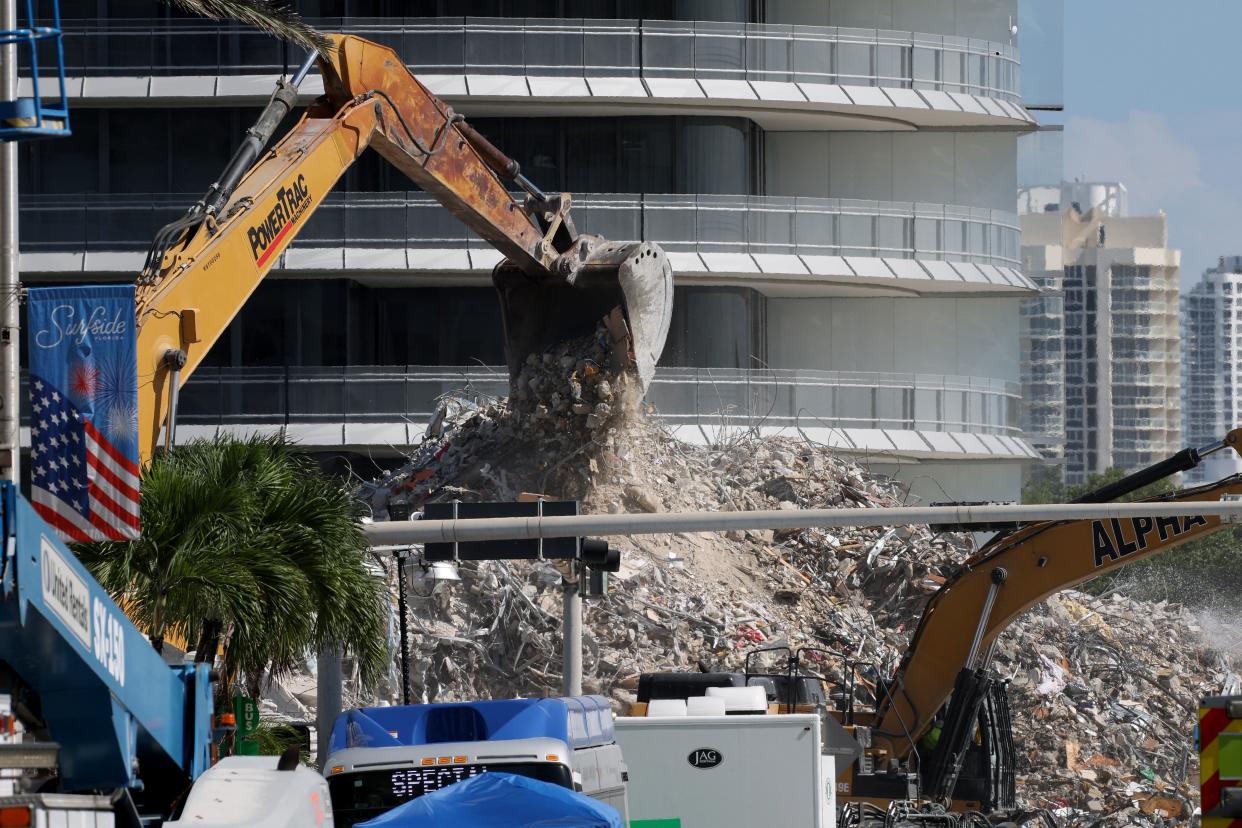 Construction equipment is used to dig through the mound of debris from the collapsed 12-story Champlain Towers South condo building is seen through fencing on July 11, 2021, in Surfside, Fla. The death toll from the collapse has risen to 90 people as the recovery operations enter its 18th day.