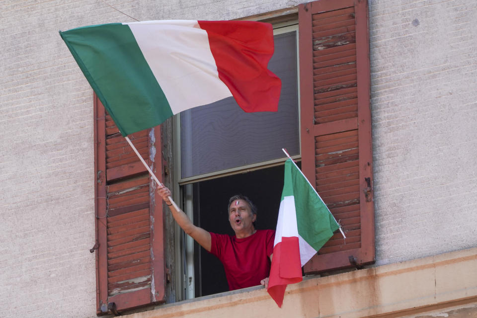 A man waves the Italian flag as he chants from his window on the occasion of the 75th anniversary of Italy's Liberation Day, in Rome, Saturday, April 25, 2020. Italy's annual commemoration of its liberation from Nazi occupation is celebrated on April 25 but lockdown measures in the coronavirus-afflicted country mean no marches can be held this year and the National Association of Italian Partisans has invited all to sing “Bella Ciao", the anthem of Italy’s communist resistance, from their windows. (AP Photo/Andrew Medichini)