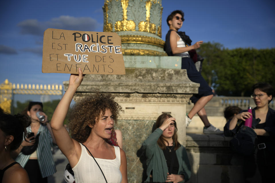 A woman holds a placard reading "Police are racist and kill children" during a protest in Paris, France, Friday, June 30, 2023. French President Emmanuel Macron urged parents Friday to keep teenagers at home and proposed restrictions on social media to quell rioting spreading across France over the fatal police shooting of a 17-year-old driver. (AP Photo/Lewis Joly)