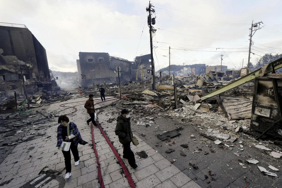 People walk past collapsed buildings following an earthquake in Wajima, Ishikawa prefecture, Japan Tuesday, Jan. 2, 2024. (Kyodo News via AP)