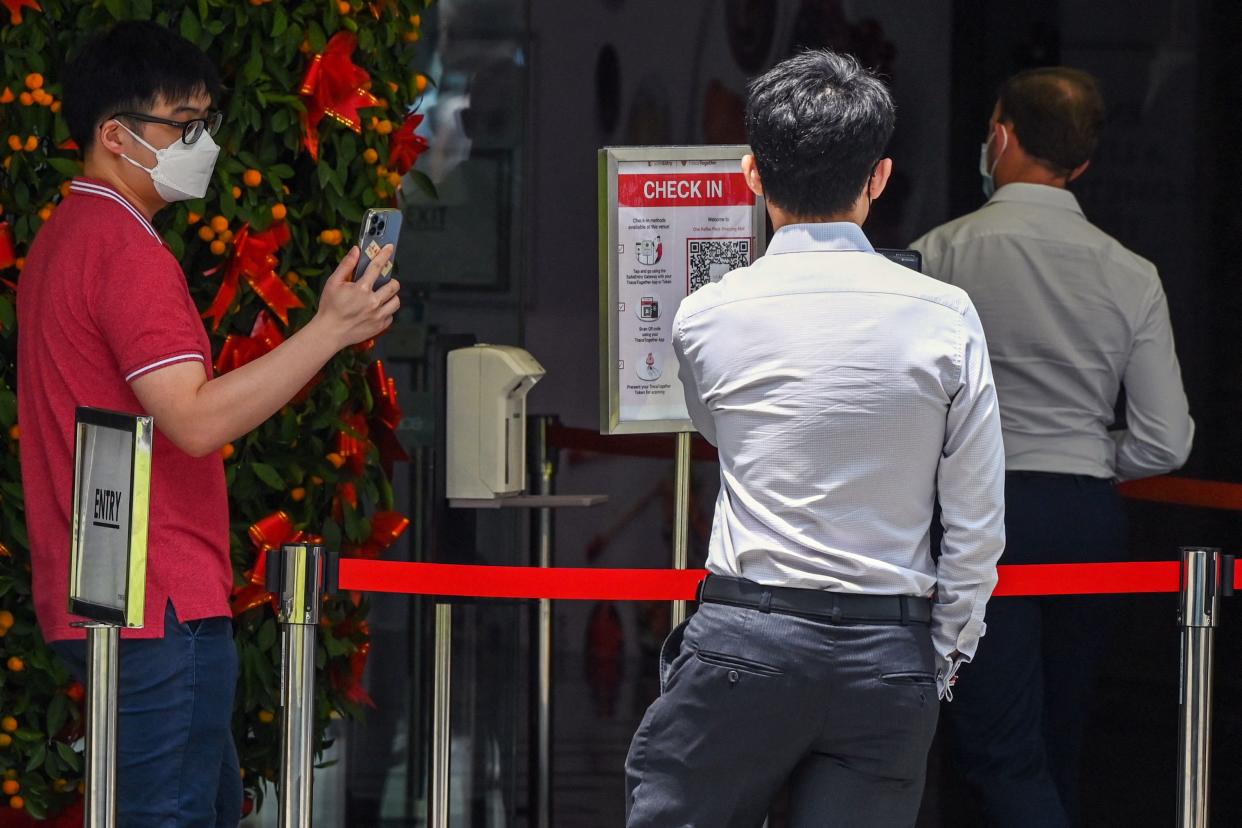 People scan a QR code using the Trace Together contact tracing app on their smartphones before entering a building at the Raffles Place financial business district in Singapore on February 14, 2022. (Photo by Roslan RAHMAN / AFP) (Photo by ROSLAN RAHMAN/AFP via Getty Images)