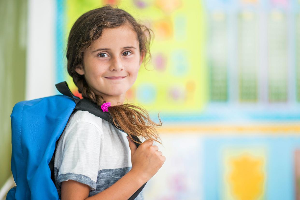 School girl standing against a wall with her backpack