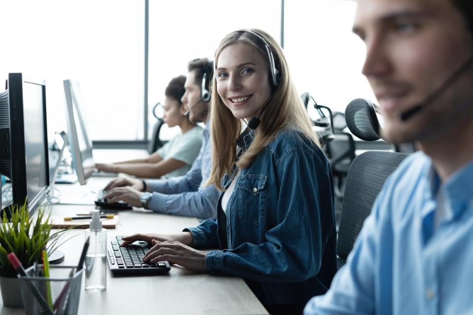 Several people working in a call center, wearing headphones and looking at computer screens.