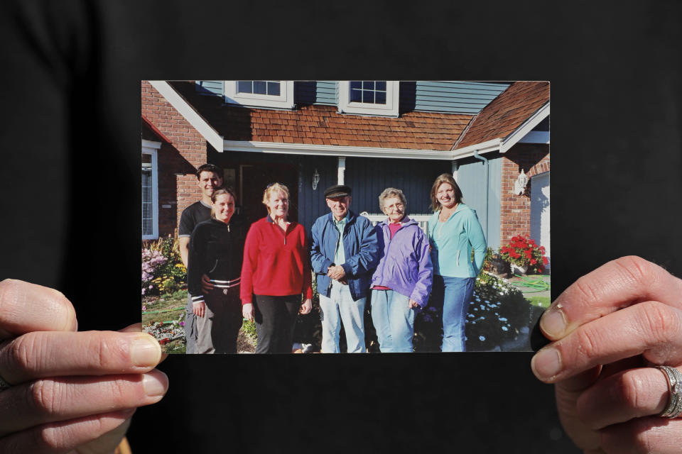 In this Wednesday, April 8, 2020, photo, Kelly Adsero holds a family photo of her grandfather Bill Chambers, center, as he stands with his wife, Barbara Jean, second from right, his daughters Patty, third from left, and Cindy, right, and Adsero and her husband Nick, left. Chambers, 97, died March 14, 2020, at an adult family home where he lived with four other World War II veterans. He wasn't obviously ill, but tested positive for the new coronavirus after he died. (AP Photo/Ted S. Warren)