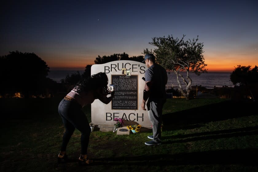 Manhattan Beach, CA - September 30: Stephanie Roberson, left, visiting from Sacramento, takes a picture, while her brother Randall Roberson, from Los Angeles, reads a plaque memorializing the park adjacent to Bruce's Beach, the evening that California Gov. Gavin Newsom signed SB 796, authorizing the return of ocean-front land to the Bruce family, at Bruce's Beach in Manhattan Beach, CA, Thursday, Sept. 30, 2021. Some of the land making up Bruce's Beach was purchased by African American couple Willa and Charles Bruce, in 1912, establishing a resort that was open to African Americans. But by the 1920s, racial tensions grew in the beach community and the city condemned the properties. The park was renamed multiple times over the next 80 years and in 2007, was re-named for the Bruce family, responsible for trying to bring change and equality to the city. (Jay L. Clendenin / Los Angeles Times)