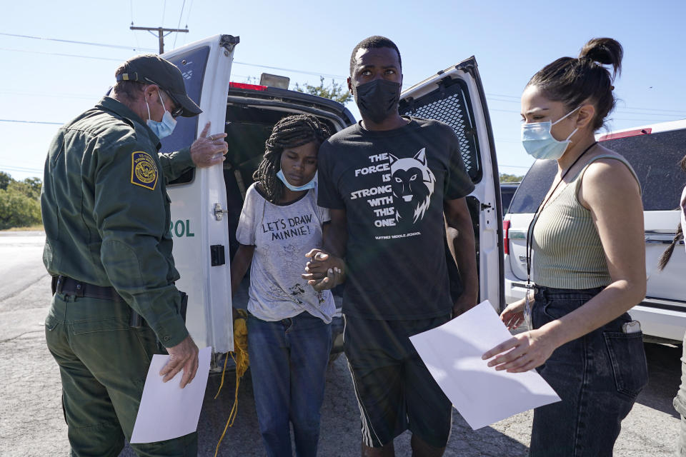 A U.S. Customs and Border Protection agent, left, drops off a migrant couple a member of of a humanitarian group, right, receives them after their release from custody, Friday, Sept. 24, 2021, in Del Rio, Texas. (AP Photo/Julio Cortez)