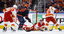 Calgary Flames goalie Jacob Markstrom, center, covers the puck as Edmonton Oilers winger Zach Hyman digs for it during the third period of Game 4 of an NHL hockey Stanley Cup playoffs second-round series Tuesday, May 24, 2022, in Edmonton, Alberta. (Jeff McIntosh/The Canadian Press via AP)
