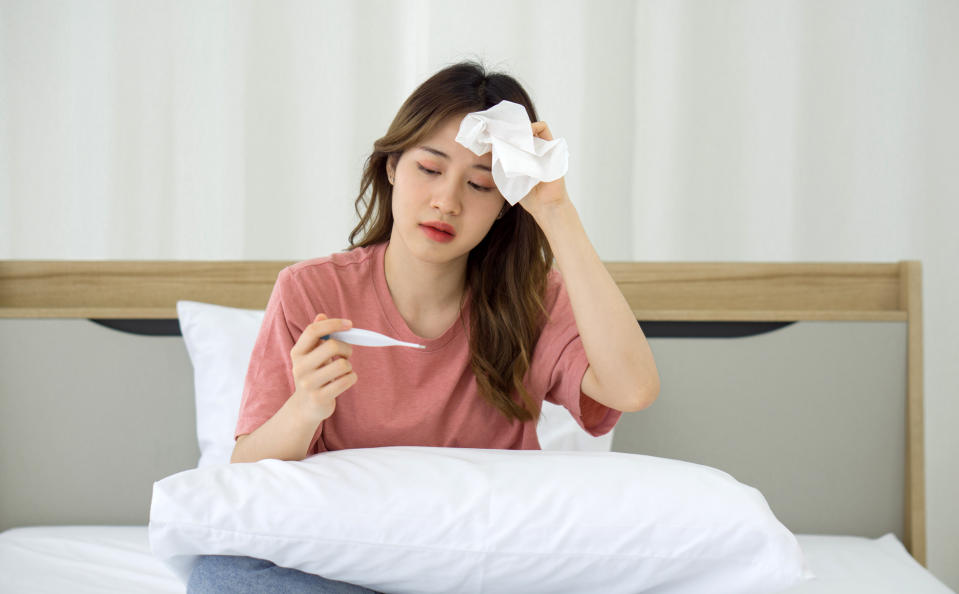 Young asian woman taking temperature with digital thermometer while sitting in bed. Covid-19 infected people stay in their rooms alone for safety, not infect people in the house.