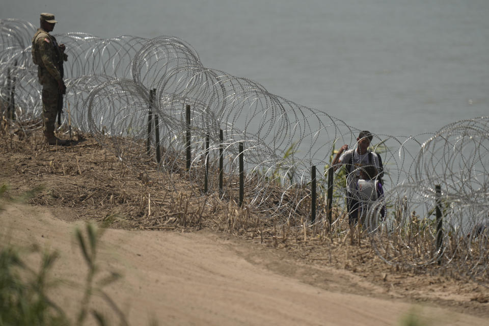 Migrantes caminan entre alambre de púas frente a un agente tras haber cruzado el río Bravo desde México, en Eagle Pass, Texas, el miércoles 12 de julio de 2023. (AP Foto/Eric Gay)