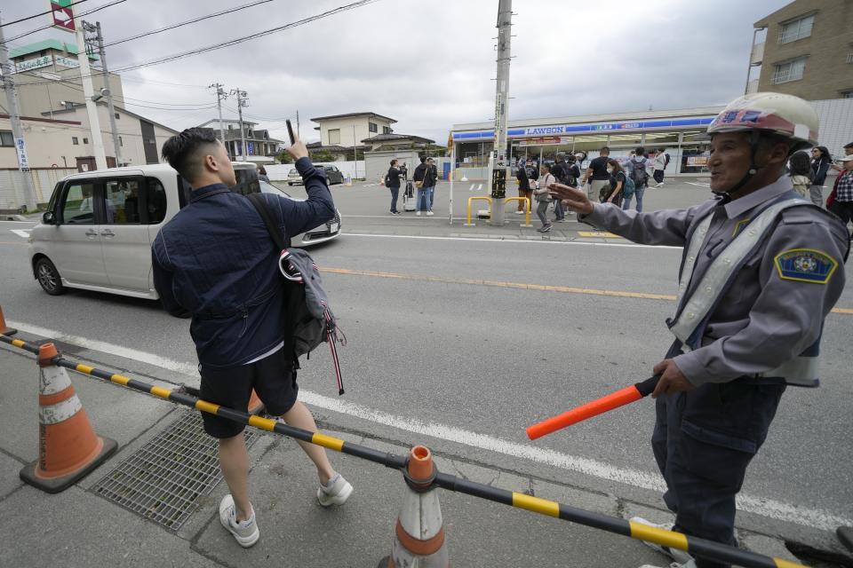 A security guard redirects a tourist outside of the construction site of a barricade near the Lawson convenience store Tuesday, April 30, 2024, at Fujikawaguchiko town, Yamanashi Prefecture, central Japan. The town of Fujikawaguchiko, known for a number of popular photo spots for Japan's trademark of Mt. Fuji, on Tuesday began to set up a huge black screen on a stretch of sidewalk to block view of the mountain in a neighborhood hit by a latest case of overtourism in Japan. (AP Photo/Eugene Hoshiko)