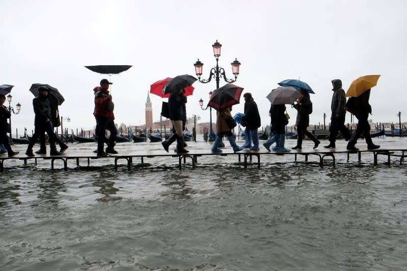 People walk on a catwalk in the flooded St. Mark's Square in Venice, Italy