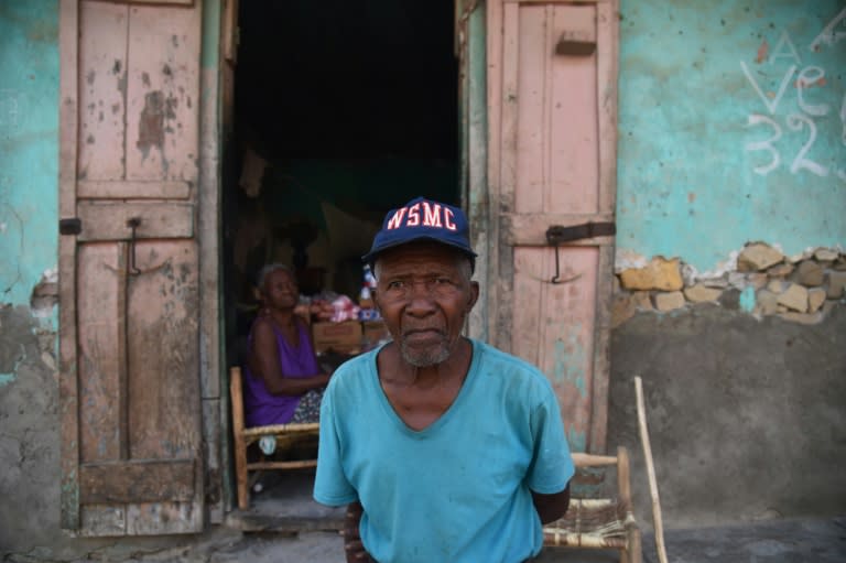 A man named Joseph poses in front a house owned by Virginie(background) that suffered some damage after the earthquake that hit the city of Port-de-Paix, on October 8, 2018