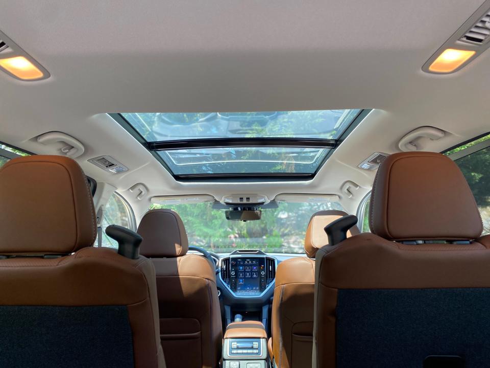 The cabin of the 2024 Subaru Ascent Touring looking forward toward the large infotainment screen from the third row through the Java Brown leather seats of the front two rows.
