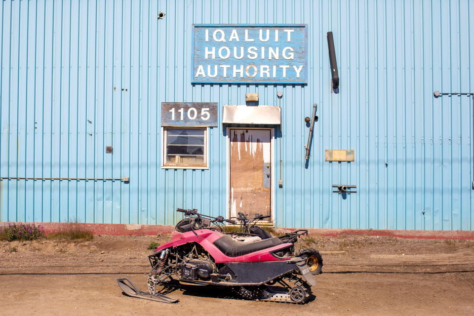 A red and black snowmobile in front of a blue building with signs reading: Iqaluit Housing Authority, 1105.