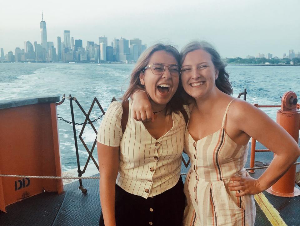 The author and her friend stand smiling on the back of the ferry with the Manhattan skyline behind them.