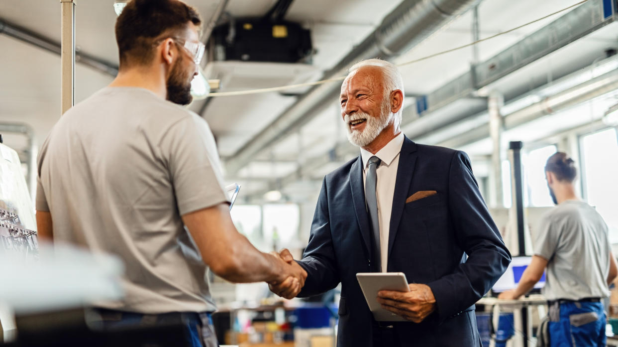 Happy senior businessman handshaking with manual worker in a factory.