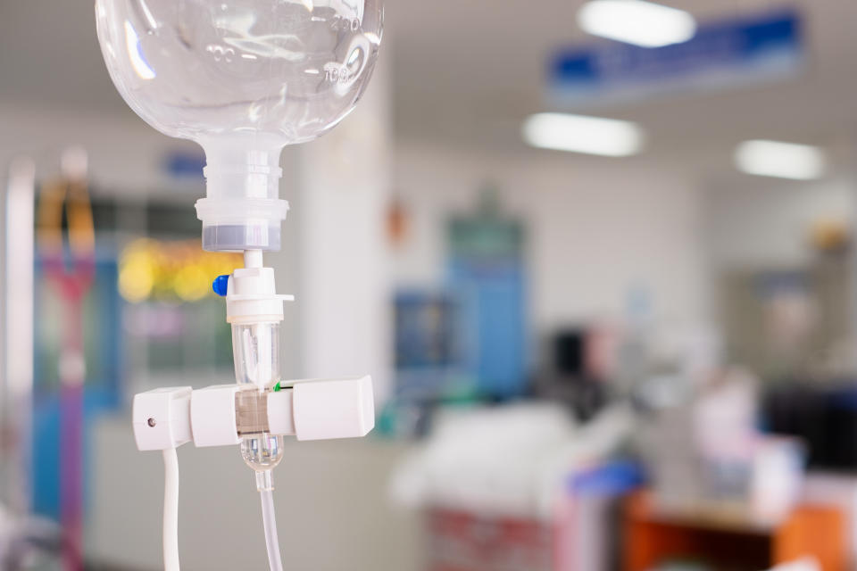 Saline Drip Hanging On Metal Hook Against Wall In Hospital