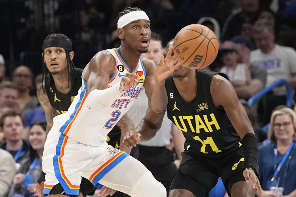 Oklahoma City Thunder guard Shai Gilgeous-Alexander (2) passes in front of Utah Jazz guard Jordan Clarkson, left, and guard Kris Dunn, right, in the first half of an NBA basketball game Sunday, March 5, 2023, in Oklahoma City. (AP Photo/Sue Ogrocki)