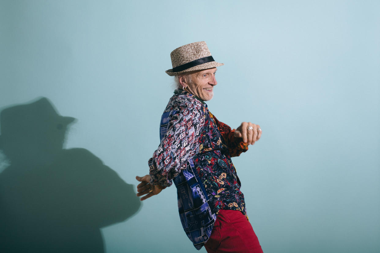 Hip senior gay man in colorful shirt dancing on a Turquoise background laughing and having fun. Part of the LGBTQ Portrait series.