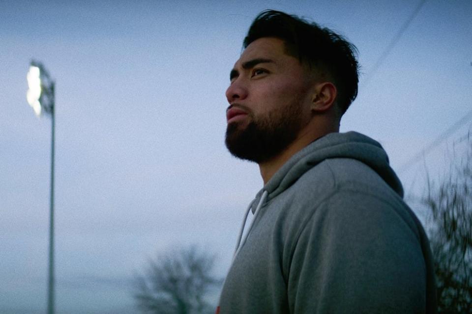 Manti Te'O wears a grey hoodie and stares off into the distance, he's outside, it's dusk, and the sky is gray