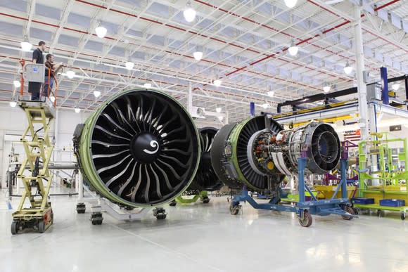 Aircraft engines in a manufacturing hangar, with a lift with workers looking at the top of the engines.