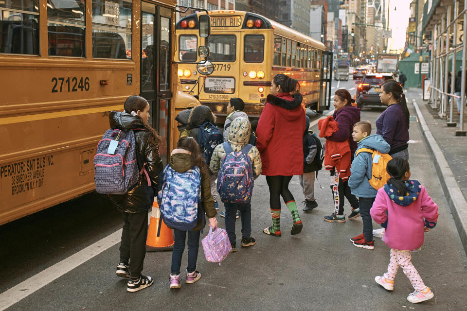 Migrant children prepare to board a school bus while guided by their guardians in front of the Row Hotel that serves as migrant shelter on Tuesday, Dec. 12, 2023, in New York. It could be a cold, grim New Year for thousands of migrant families living in New York City’s emergency shelter system. With winter setting in, they are being told they need to clear out, with no guarantee they’ll be given a bed elsewhere. (AP Photo/Andres Kudacki)