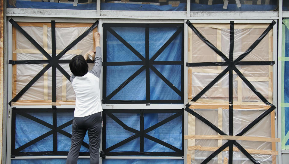 A woman takes windows in preparation for Typhoon Hagibis, in Kyonan town, Chiba prefecture, near Tokyo Friday, Oct. 11, 2019. A powerful typhoon is forecast to bring up to 80 centimeters (31 inches) of rain and damaging winds to the Tokyo area and Japan's Pacific coast this weekend, and the government is warning residents to stockpile necessities and leave high-risk places before it's too dangerous. (Naoya Osato/Kyodo News via AP)