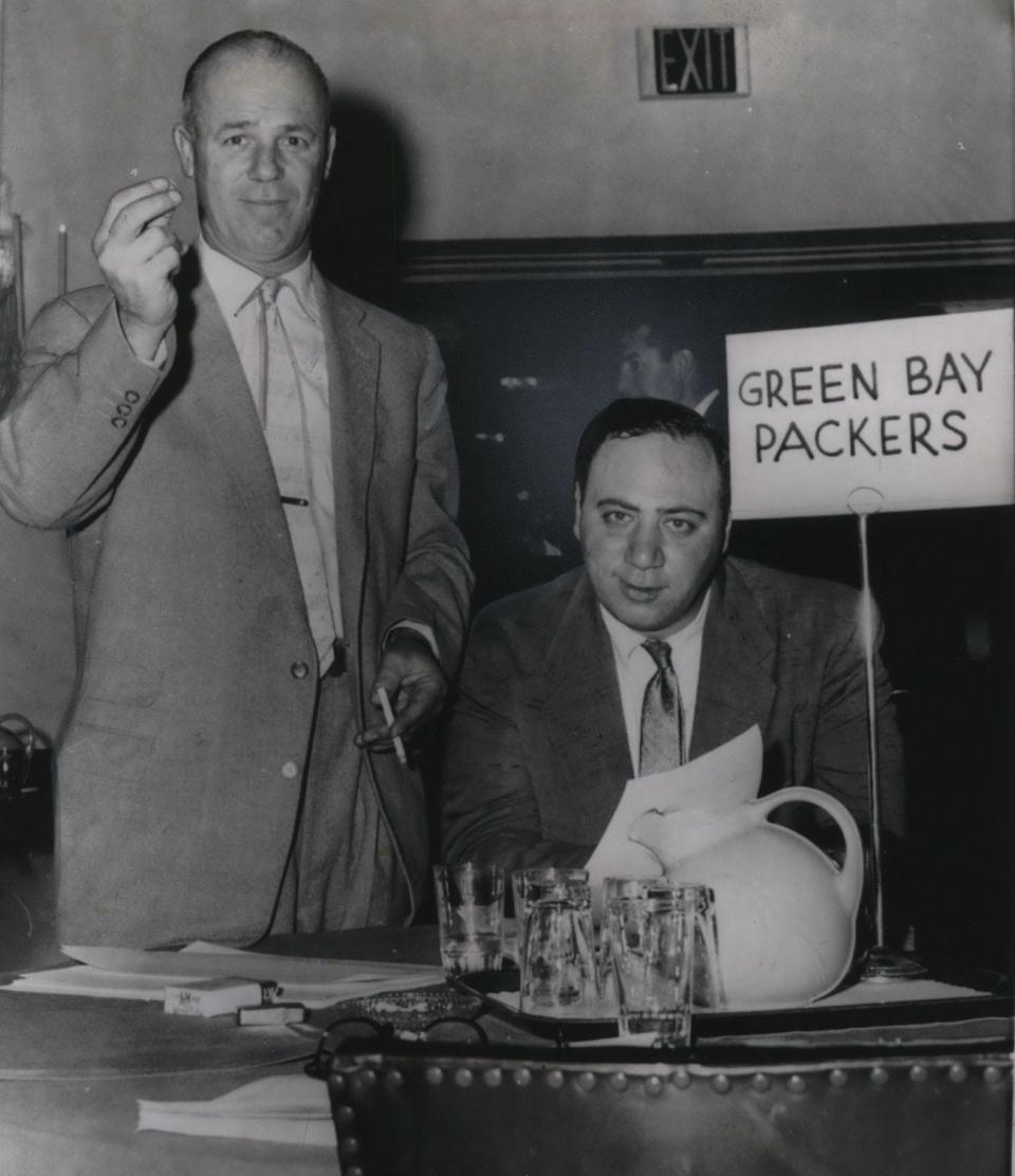 Packers coach Ray (Scooter) McLean (left), with Packers chief scout Jack Vainisi, raises his hand in making the first choice in the 1959 NFL draft in Philadelphia. The Packers chose Randy Duncan of Iowa.