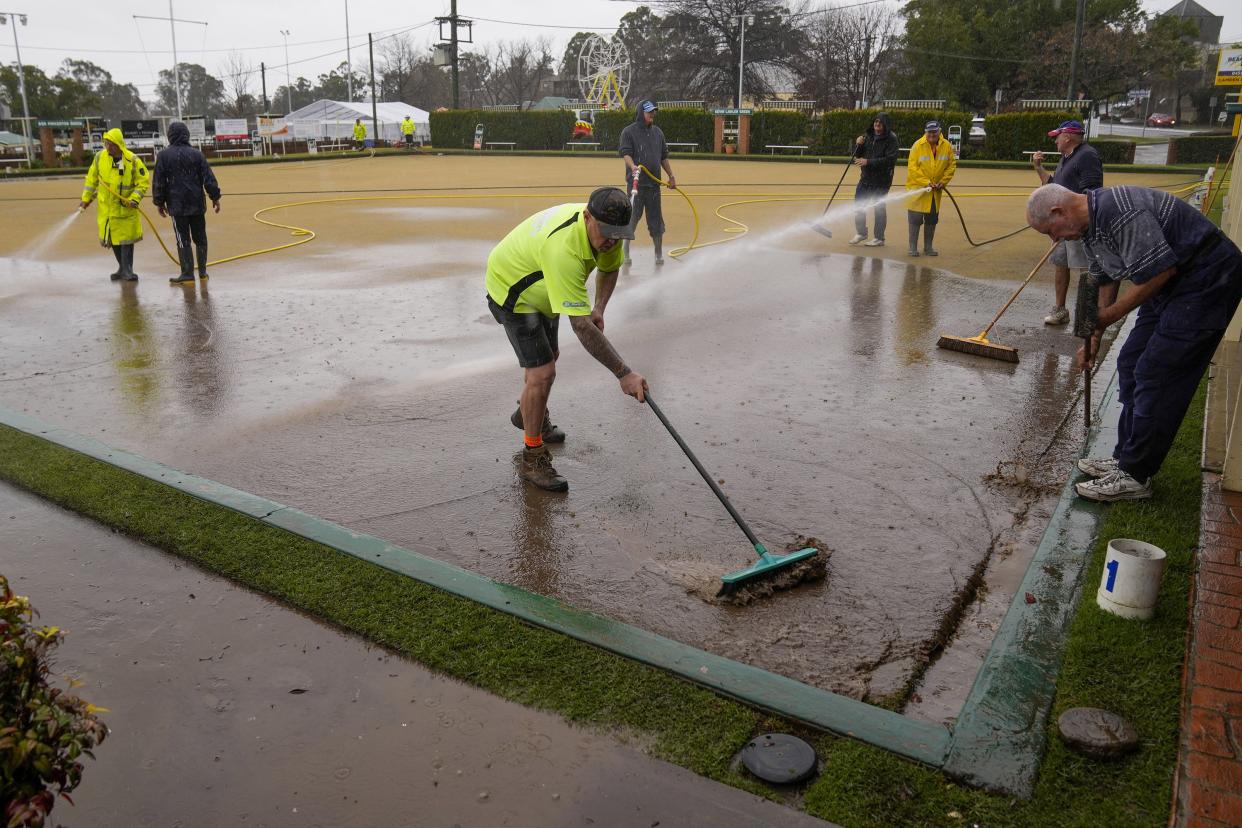 Workers clear mud from a bowling green at Camden on the outskirts of Sydney, Australia, Monday, July 4, 2022.